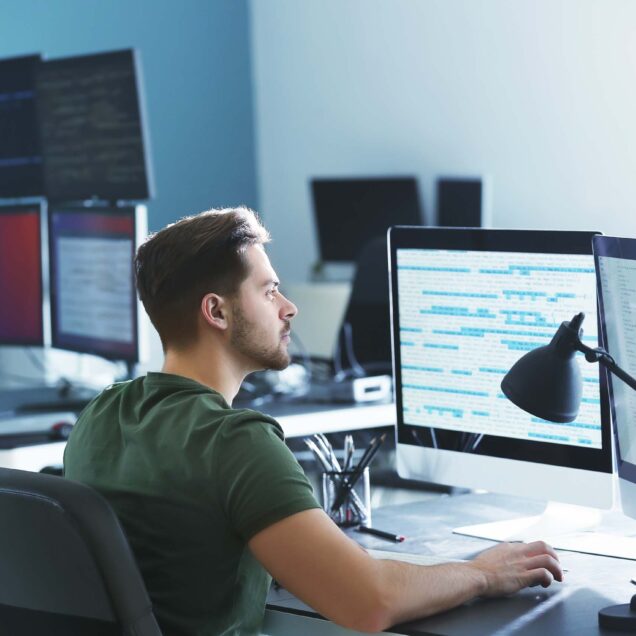 Employee reviewing code on two monitors